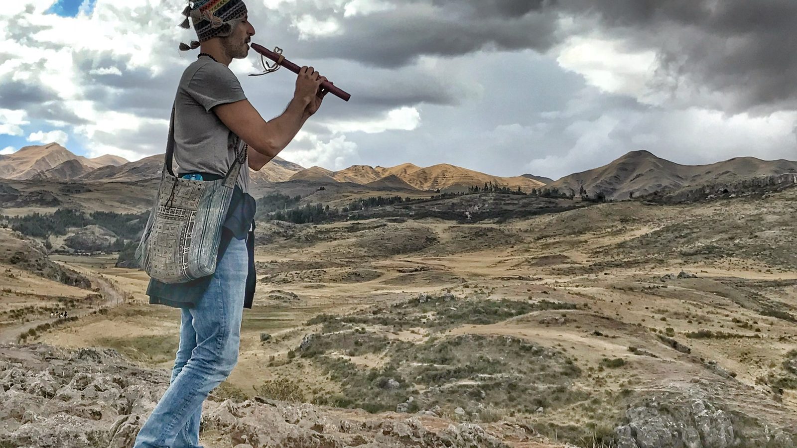 Someone standing on rock high above a valley, playing a wooden flute