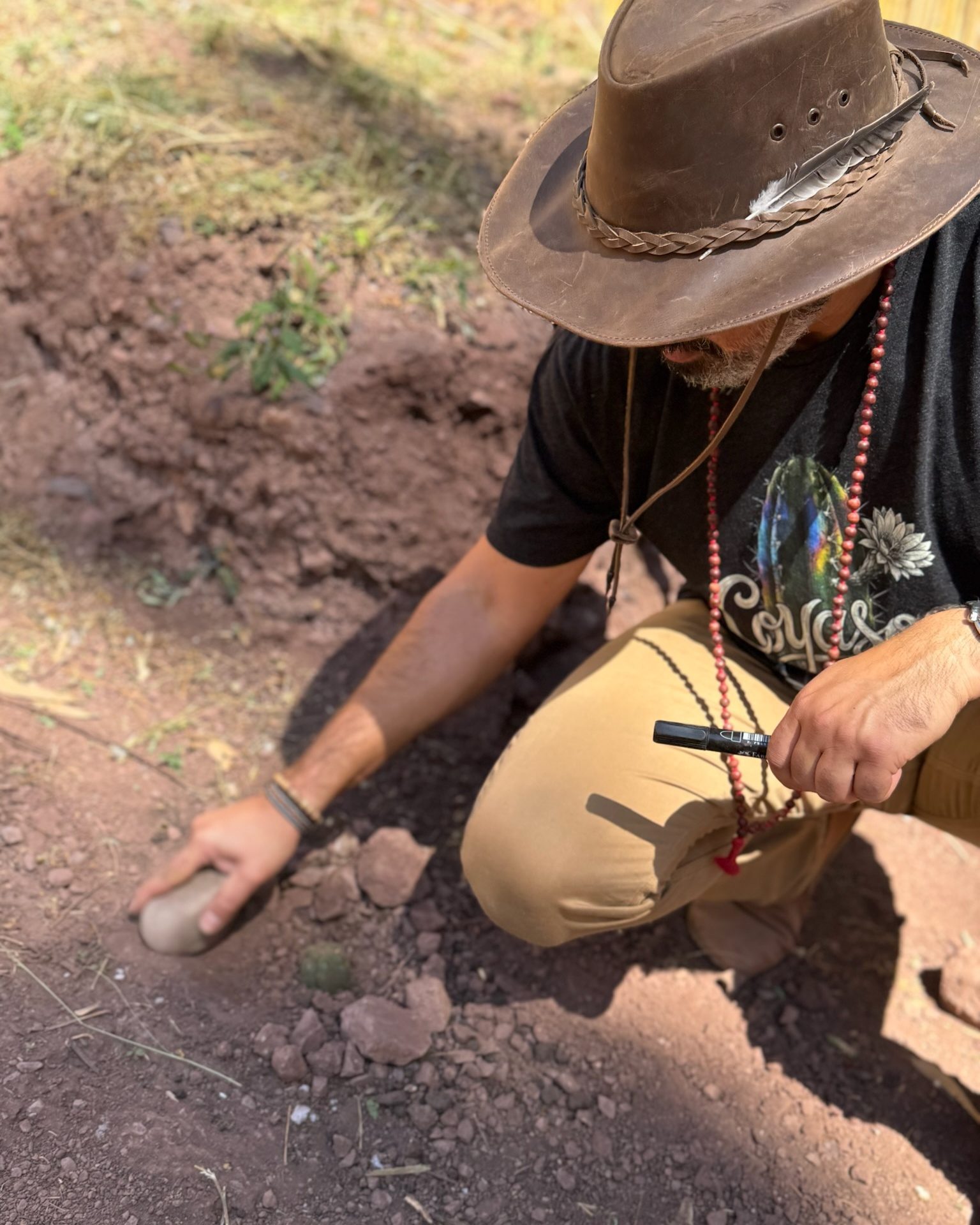 Someone in a wide brimmed hat kneeling to set a huachuma cutting into the earth at the Sanctuary