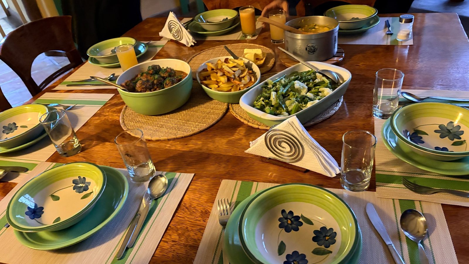 A long table laid with painted bowls of food, plates and glasses, set for a group