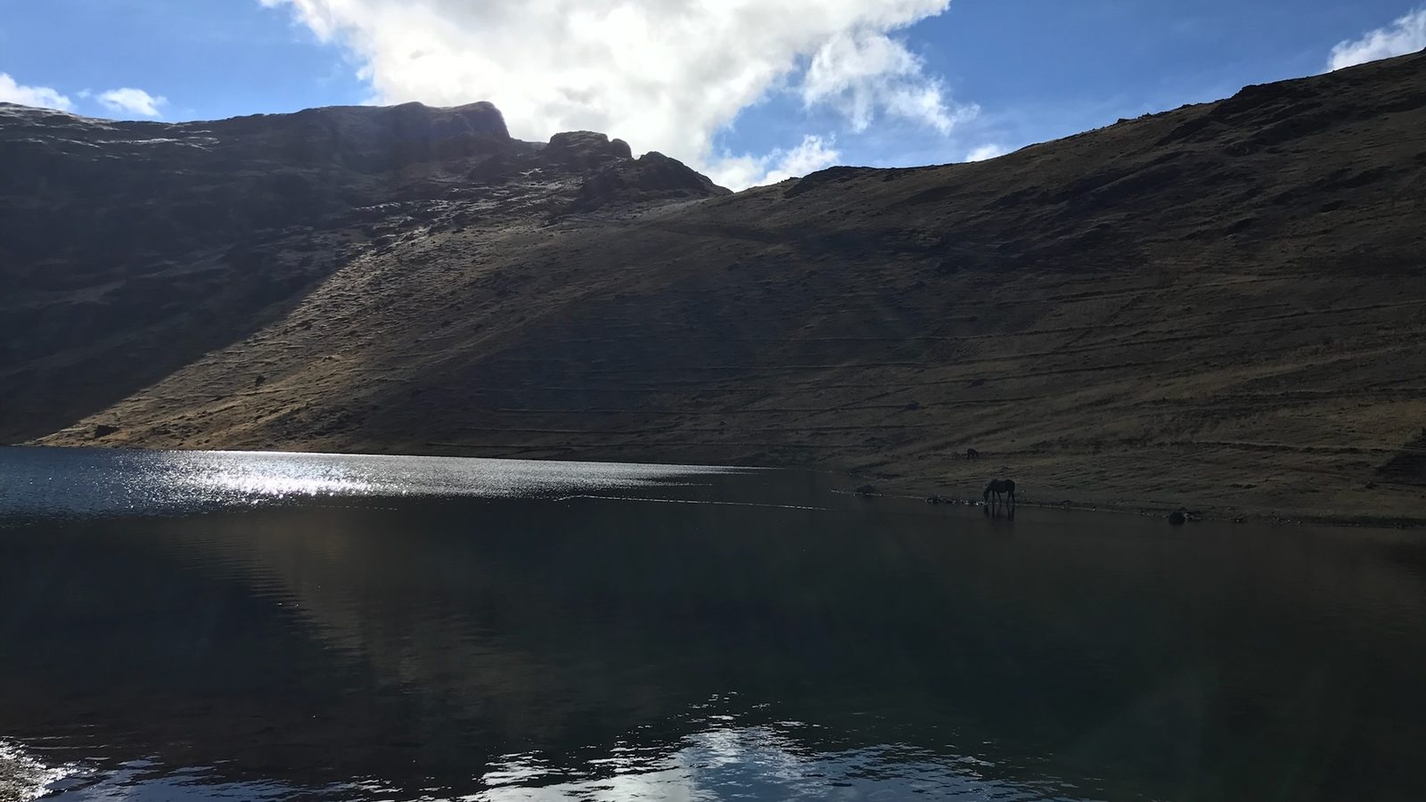 A still lake holding the reflection of a dark mountain and a bank of cloud