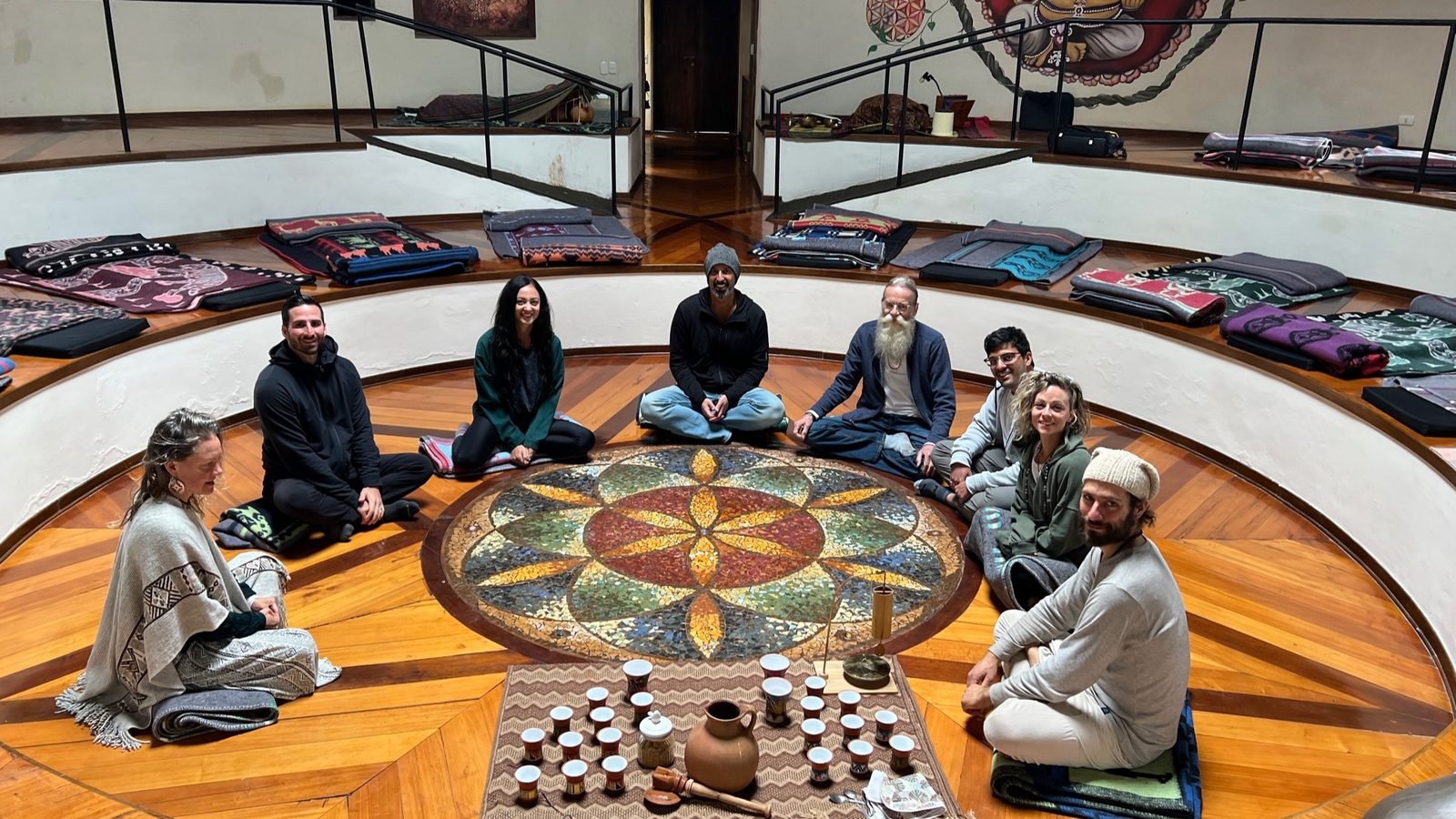 People sitting in a circle on the floor around a painted mandala set with singing bowls