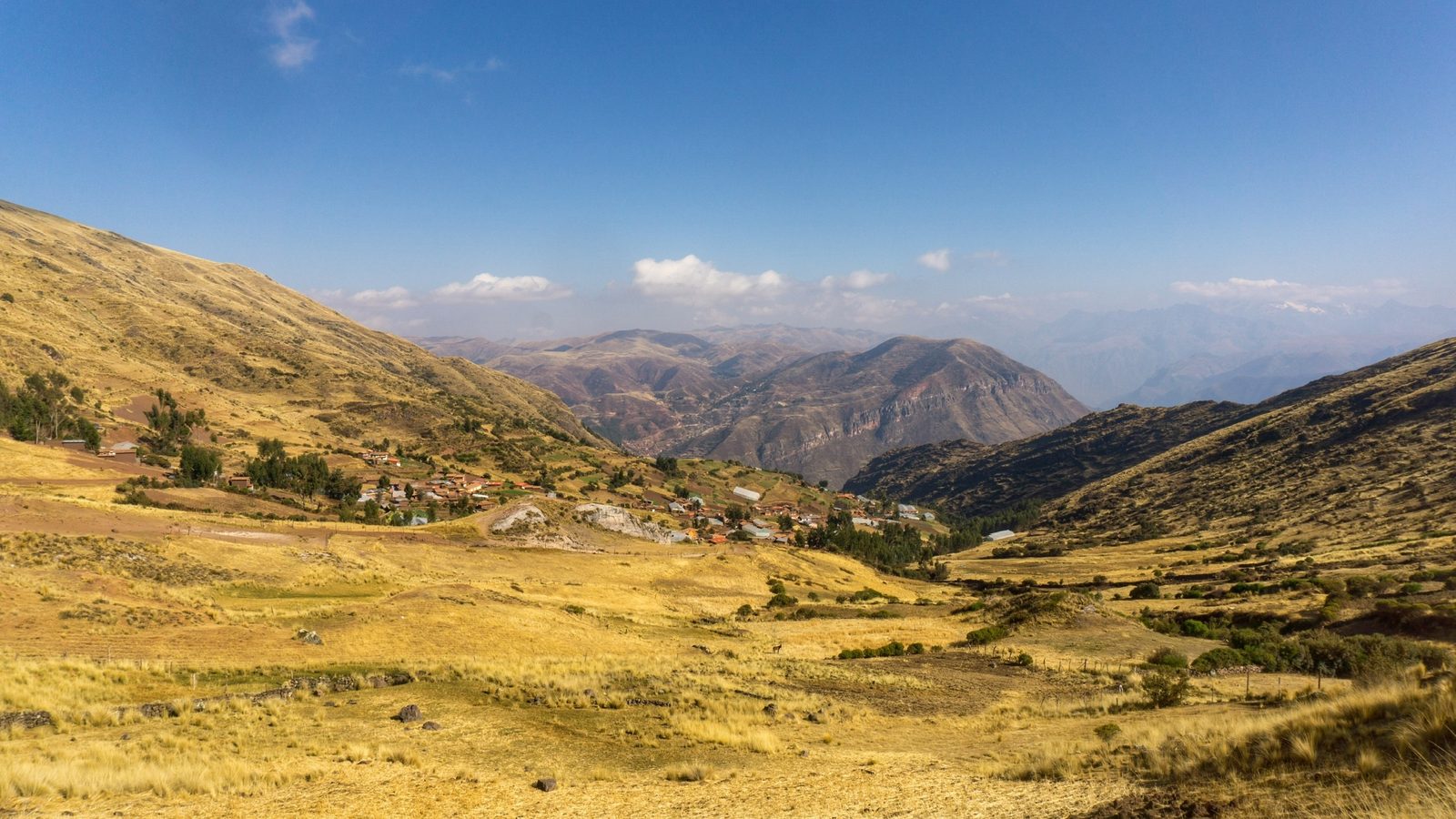 A wide valley of golden grassland falling away to mountains under a high sky