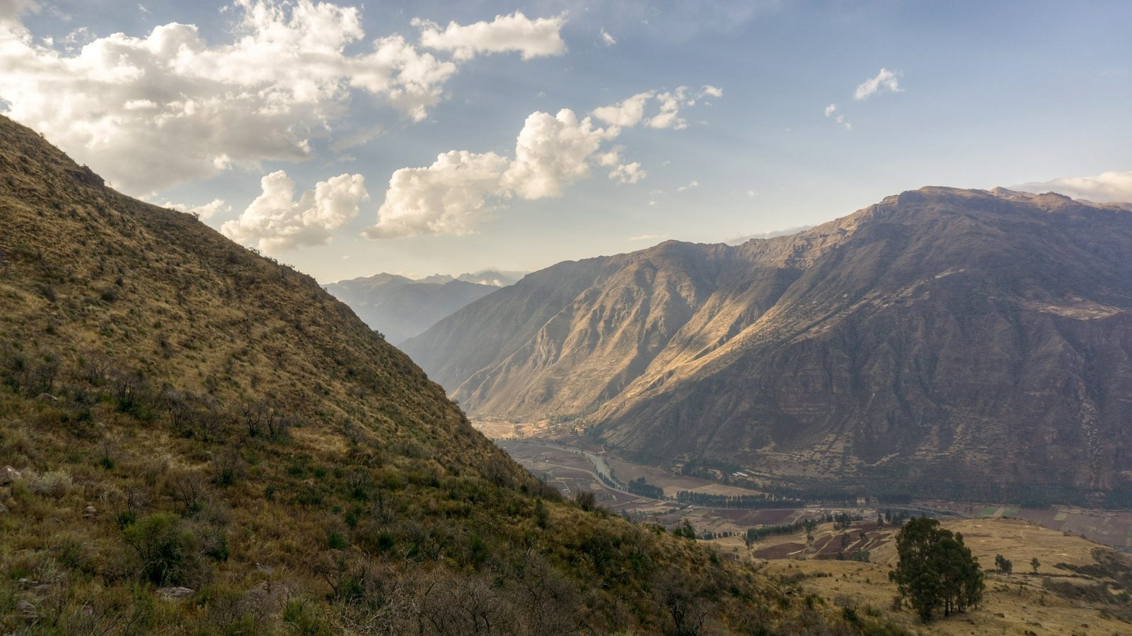 A steep valley of dry grass and rock falling towards distant mountains