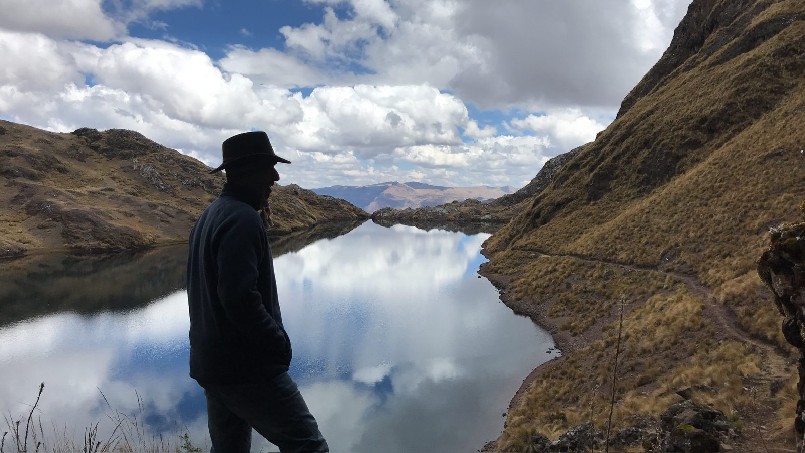 Someone walking the shore of a mirror still lake between two dark hills on a ceremony day