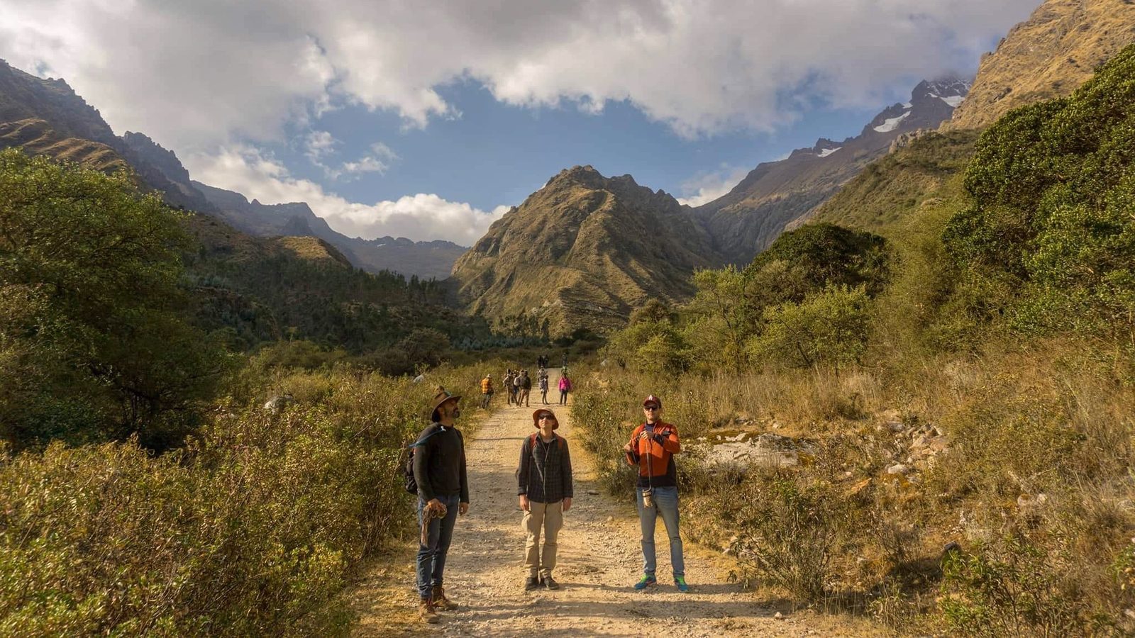 Three walkers standing on a trail with a wide valley and mountains behind them